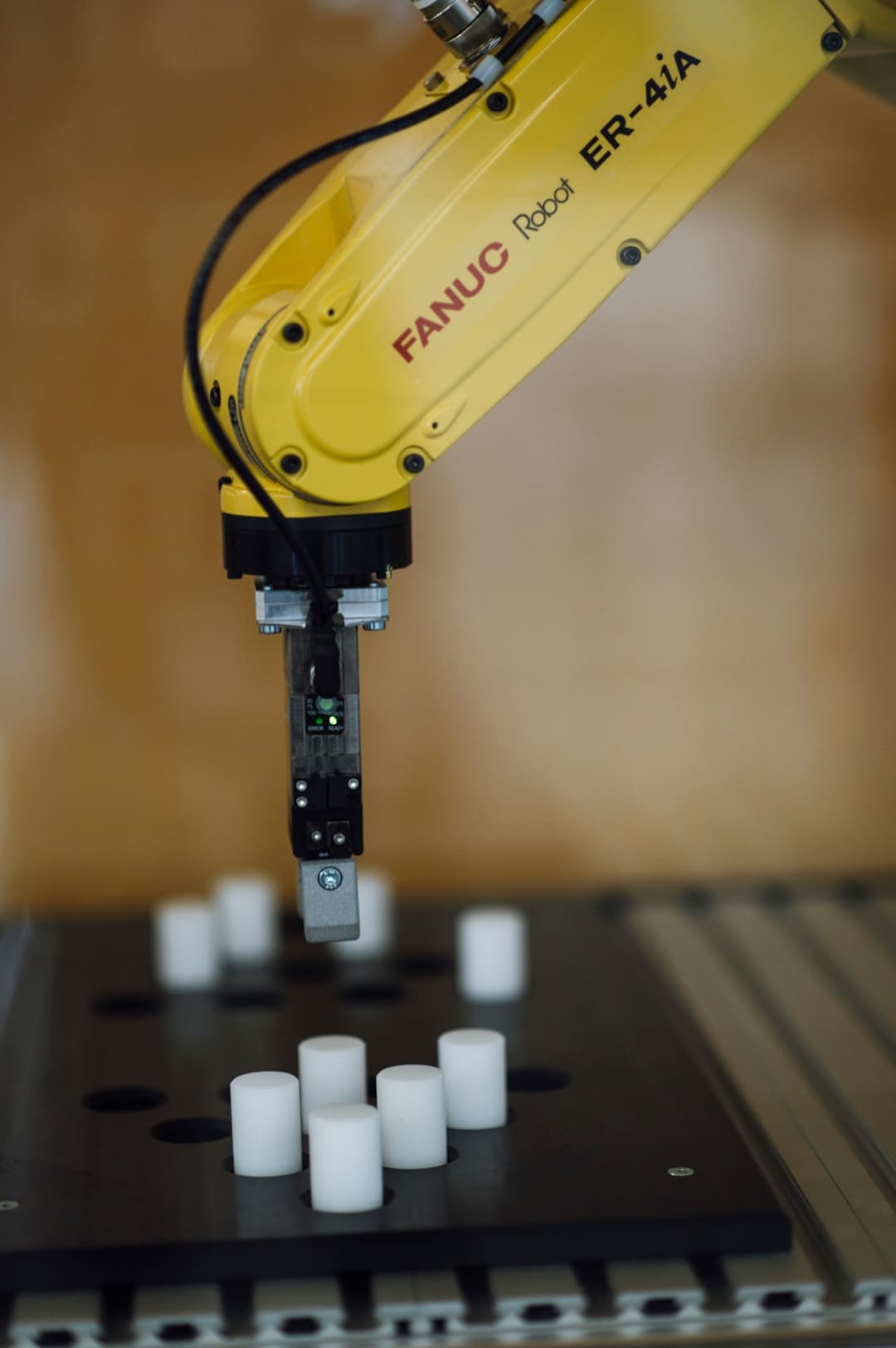 Geltona FANUC ER-4iA robotinė ranka gamykloje ima baltus cilindrus
